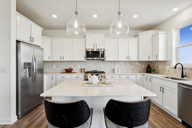 kitchen with a kitchen island, appliances with stainless steel finishes, white cabinetry, pendant lighting, and a sink