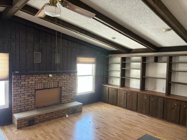 living area featuring a fireplace, vaulted ceiling with beams, light wood finished floors, wood walls, and a textured ceiling