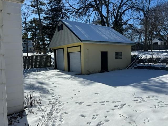 snow covered garage featuring a garage and fence