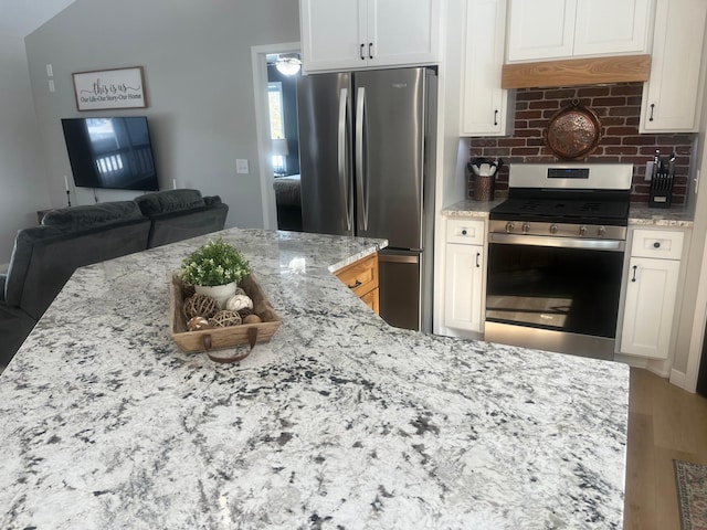 kitchen featuring light stone counters, white cabinets, appliances with stainless steel finishes, tasteful backsplash, and open floor plan