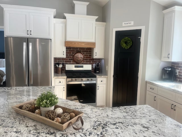 kitchen with tasteful backsplash, white cabinets, appliances with stainless steel finishes, and light stone countertops