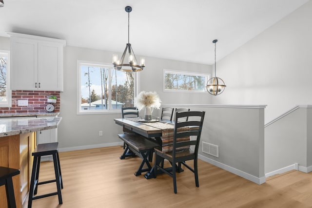 dining space with baseboards, visible vents, a chandelier, vaulted ceiling, and light wood-style floors