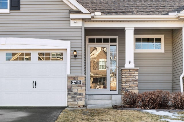 property entrance featuring stone siding, aphalt driveway, and roof with shingles