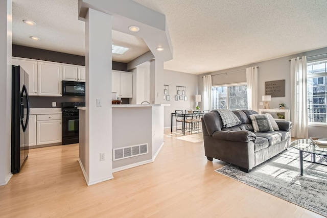 living room with baseboards, a textured ceiling, visible vents, and light wood-style flooring