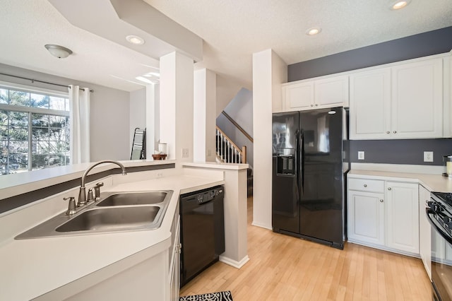 kitchen with a sink, light countertops, light wood-style flooring, white cabinetry, and black appliances