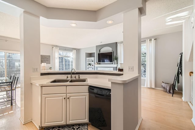kitchen featuring a sink, light countertops, light wood finished floors, open floor plan, and black dishwasher