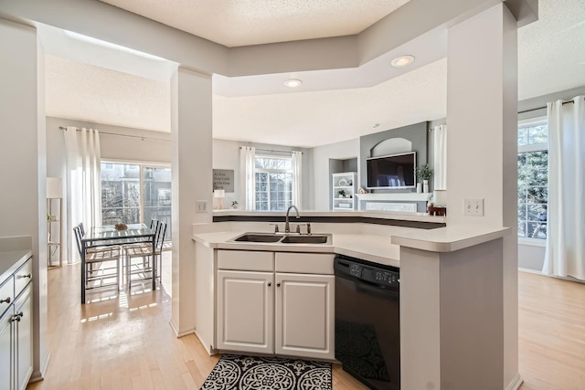 kitchen with a sink, light countertops, black dishwasher, and light wood finished floors