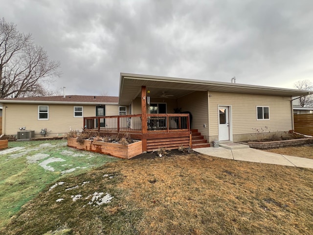 rear view of property featuring a deck, a lawn, a garden, and central air condition unit