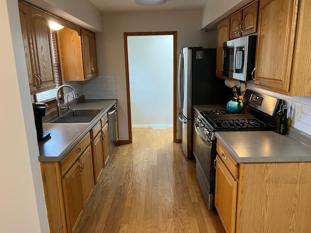 kitchen featuring a sink, appliances with stainless steel finishes, light wood-type flooring, backsplash, and dark countertops