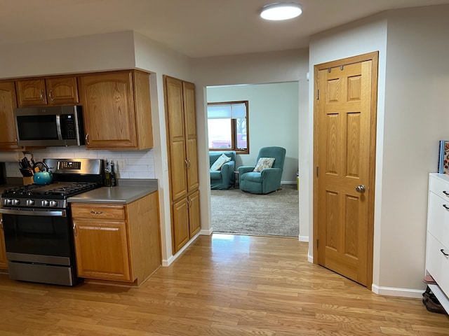 kitchen featuring baseboards, appliances with stainless steel finishes, backsplash, light wood finished floors, and brown cabinetry