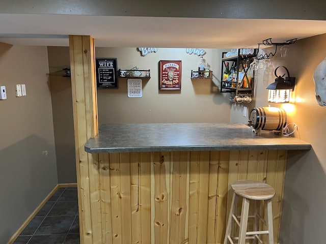 bar with a bar, dark tile patterned floors, and baseboards