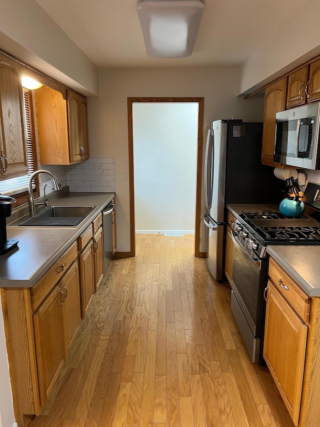 kitchen featuring light wood-style flooring, a sink, appliances with stainless steel finishes, brown cabinetry, and dark countertops