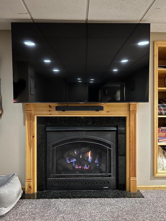 room details featuring carpet floors, a lit fireplace, baseboards, and a drop ceiling