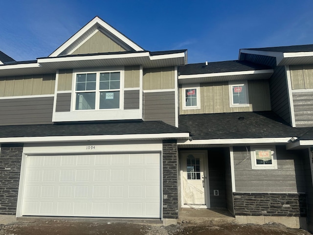 multi unit property with an attached garage, stone siding, and roof with shingles