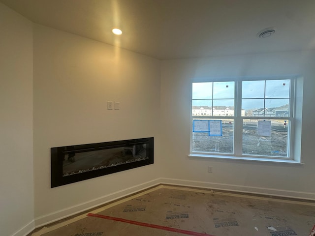 empty room with a glass covered fireplace, recessed lighting, baseboards, and visible vents