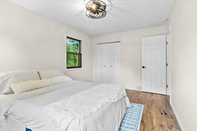 bedroom with light wood-style floors, visible vents, baseboards, and a closet