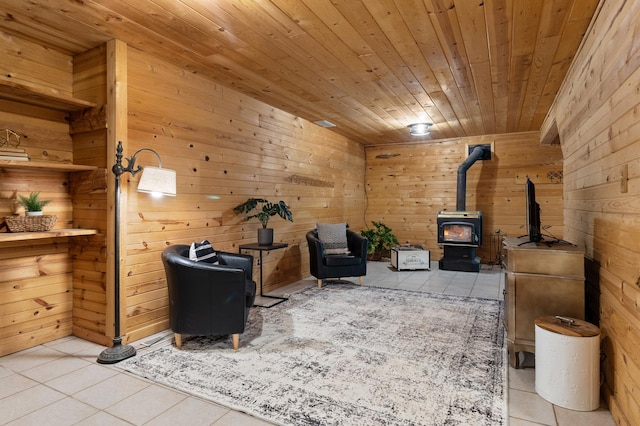 sitting room with wood ceiling, light tile patterned floors, a wood stove, and wooden walls