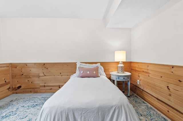 bedroom featuring light tile patterned floors, wainscoting, and wooden walls