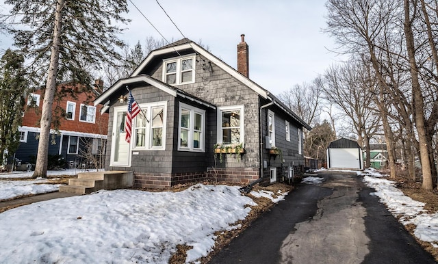 bungalow featuring a detached garage, a chimney, an outdoor structure, and driveway