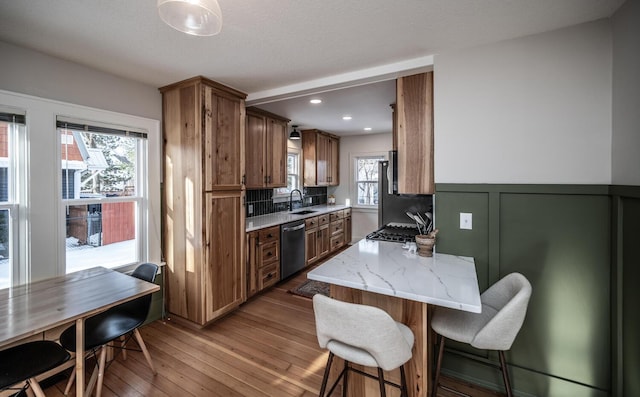 kitchen featuring a wainscoted wall, dishwasher, a kitchen breakfast bar, hardwood / wood-style flooring, and a sink