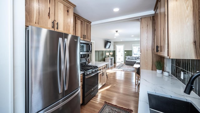 kitchen with light stone countertops, a sink, stainless steel appliances, open floor plan, and light wood-type flooring