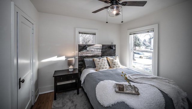 bedroom featuring baseboards, multiple windows, wood finished floors, and a ceiling fan