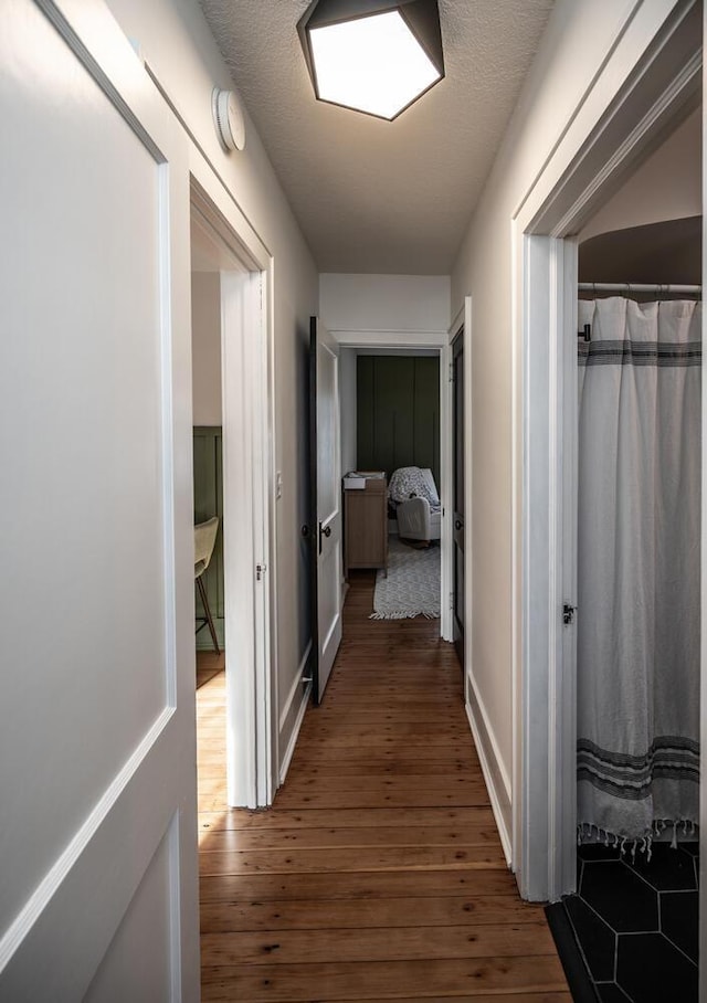 hallway featuring dark wood finished floors, a textured ceiling, and baseboards