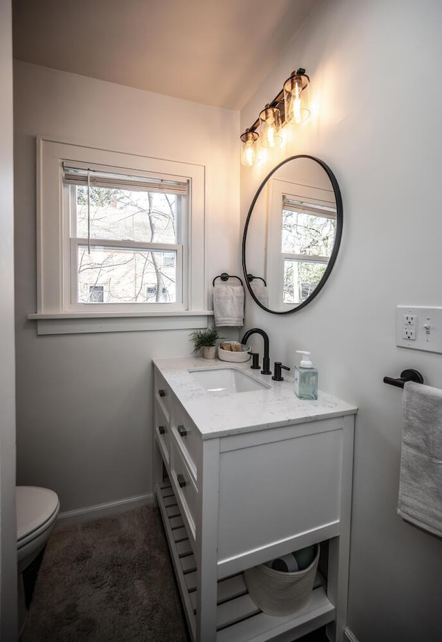 half bathroom featuring toilet, vanity, and baseboards