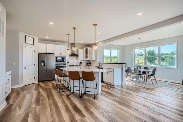 kitchen with stainless steel appliances, light countertops, glass insert cabinets, white cabinetry, and wall chimney exhaust hood