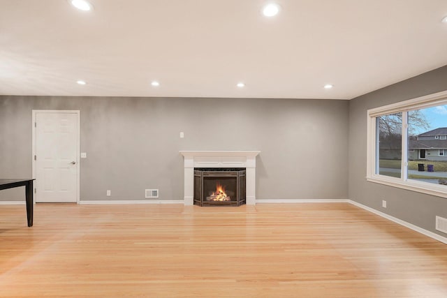 unfurnished living room featuring light wood-style floors, a lit fireplace, visible vents, and recessed lighting