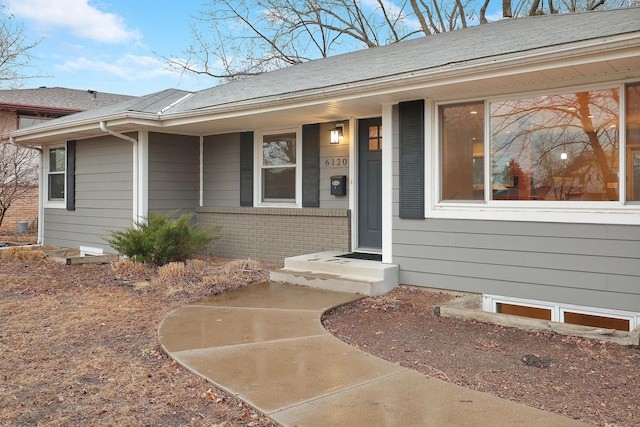 view of exterior entry with a shingled roof and brick siding