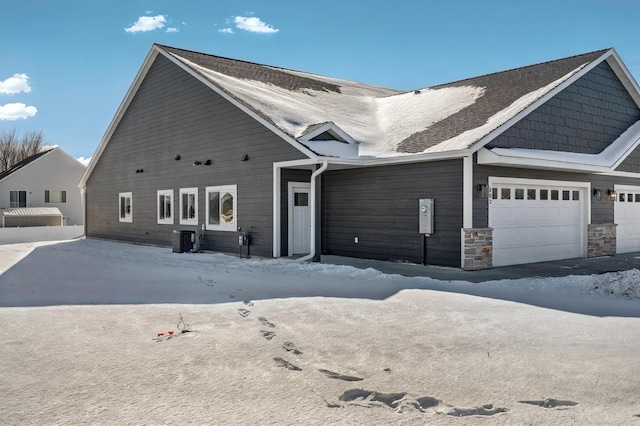 view of front facade with a garage, stone siding, and cooling unit