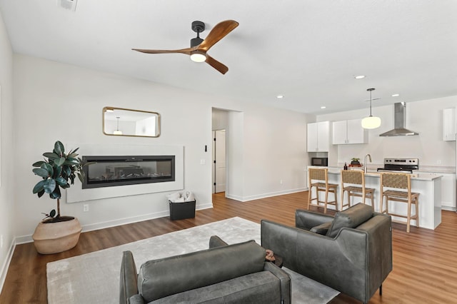 living area with recessed lighting, a ceiling fan, a glass covered fireplace, wood finished floors, and baseboards