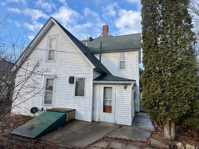 rear view of property with roof with shingles, a chimney, and a patio