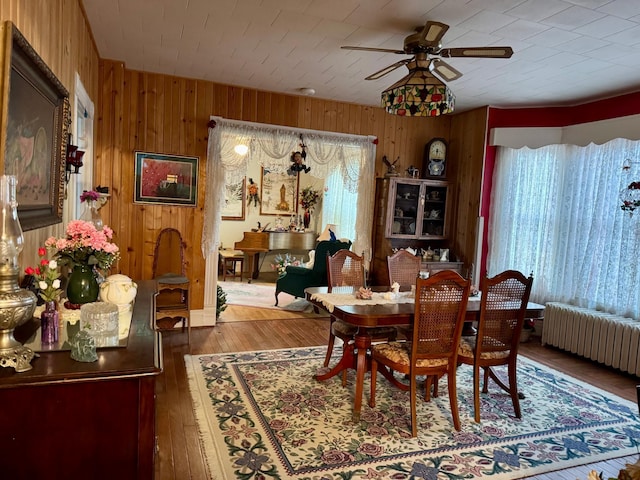 dining room featuring radiator, hardwood / wood-style flooring, ceiling fan, and wood walls