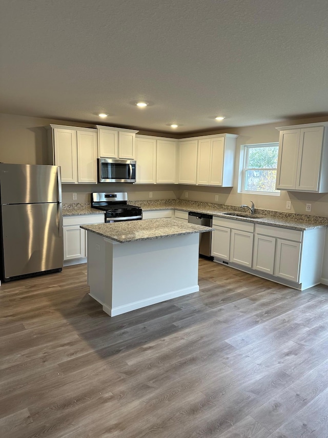 kitchen featuring a center island, appliances with stainless steel finishes, white cabinetry, a sink, and light stone countertops