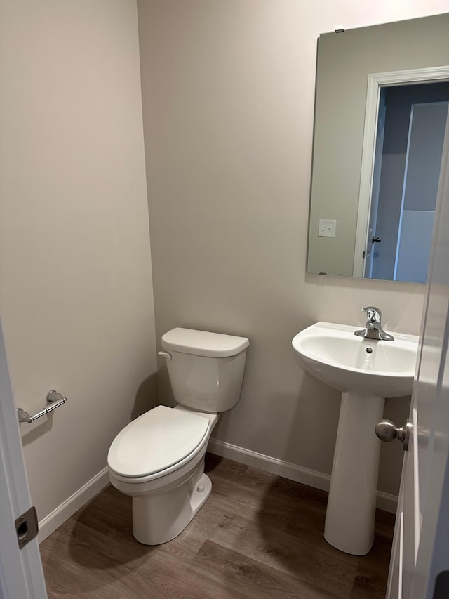 half bathroom featuring wood finished floors, toilet, and baseboards