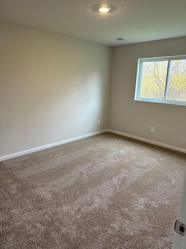 carpeted empty room featuring a textured ceiling and baseboards