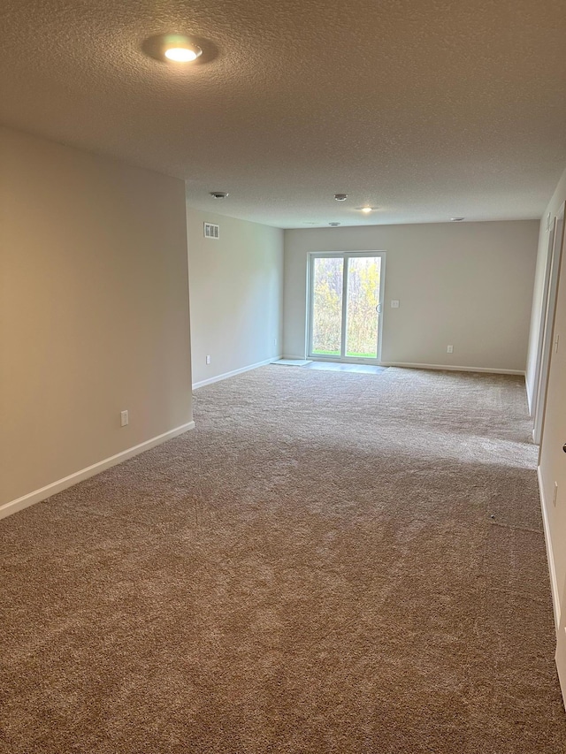 spare room featuring a textured ceiling, carpet, visible vents, and baseboards