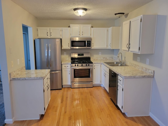 kitchen featuring appliances with stainless steel finishes, light countertops, light wood-style floors, white cabinetry, and a sink