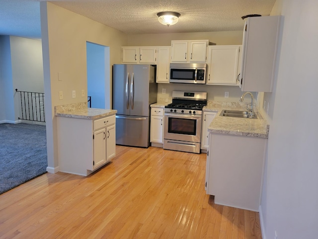 kitchen featuring light wood finished floors, white cabinets, stainless steel appliances, light countertops, and a sink