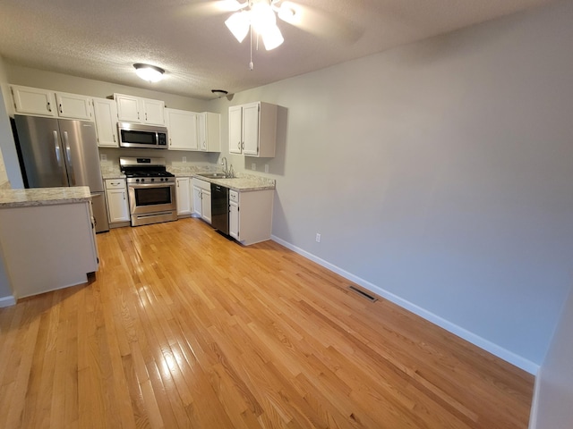 kitchen with a sink, white cabinetry, baseboards, light wood-style floors, and appliances with stainless steel finishes