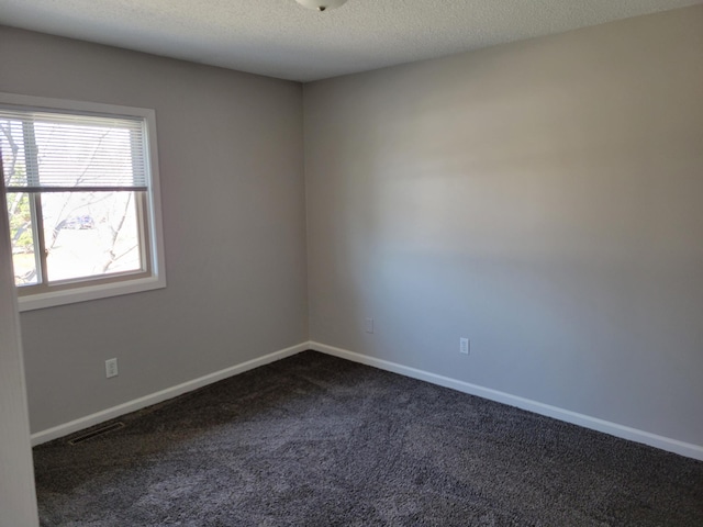 empty room with a textured ceiling, dark carpet, visible vents, and baseboards