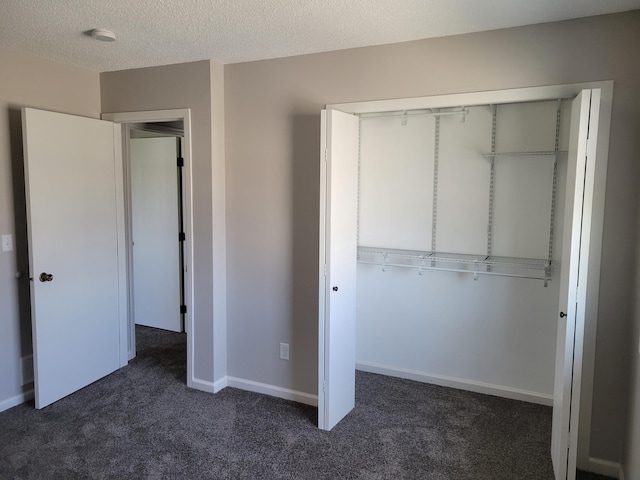 unfurnished bedroom featuring a closet, dark carpet, a textured ceiling, and baseboards