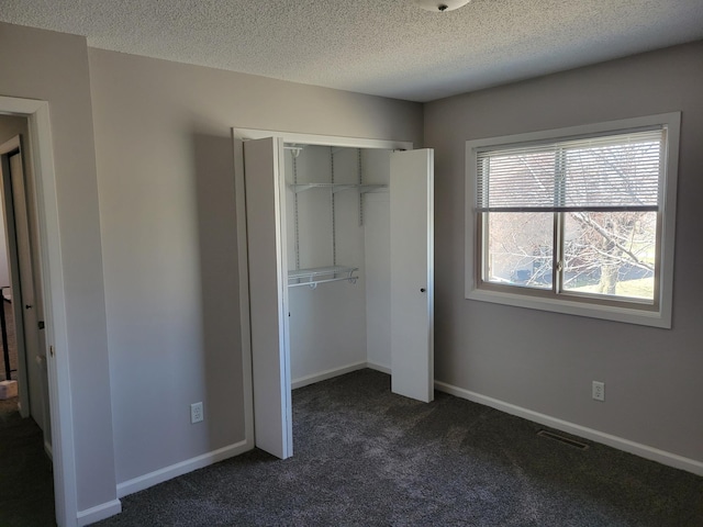 unfurnished bedroom featuring a closet, visible vents, dark carpet, a textured ceiling, and baseboards