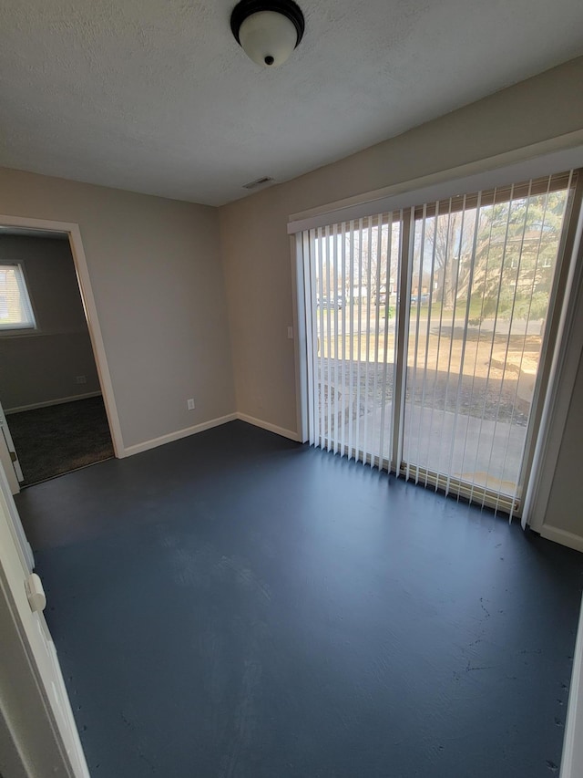 spare room featuring concrete flooring, visible vents, a textured ceiling, and baseboards