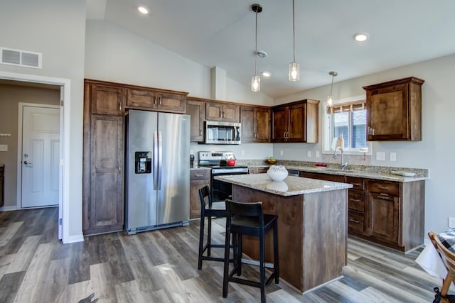 kitchen with a kitchen island, visible vents, appliances with stainless steel finishes, light stone countertops, and decorative light fixtures