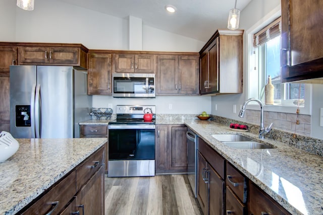 kitchen with light stone counters, decorative light fixtures, vaulted ceiling, stainless steel appliances, and a sink