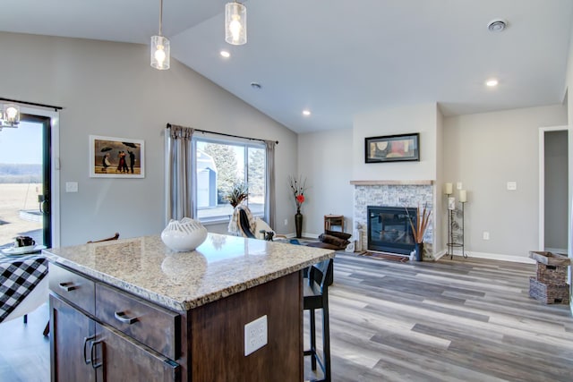 kitchen featuring a stone fireplace, light wood-style floors, dark brown cabinets, a center island, and pendant lighting