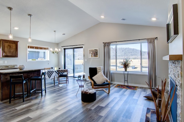 living area featuring a chandelier, a stone fireplace, wood finished floors, baseboards, and vaulted ceiling